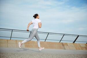 Aussicht von das zurück zu ein Sportlerin, Läufer Jogger Athlet tun Cardio trainieren, Laufen draußen auf das Stadt Brücke foto