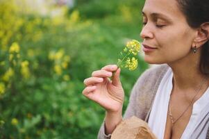 Nahansicht ziemlich Frau, ein Botaniker Kräuterkenner schnüffeln ein Blume während Sammeln medizinisch Kräuter im das Berge draußen foto