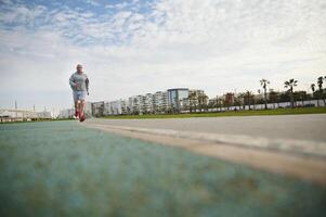 gut aussehend Sportler, sportlich Mann Laufen auf das Brücke auf sonnig Tag, genießen seine Morgen Joggen auf das Promenade foto