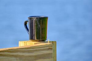 ein Kaffee Tasse auf das Kante von das Deck mit das Golf von Mexiko im das Hintergrund foto