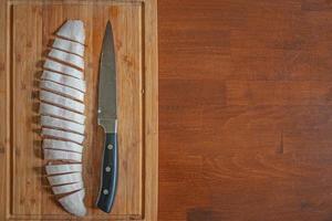 halbgefrorener Fisch auf einem Holzbrett, das mit einem großen Messer auf feine Scheiben geschnitten wurde, Details, Nahaufnahme, mit Kopienraum als Holztischplatte. Konzept Hausmannskost und gesundes Essen. foto