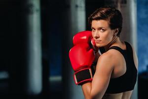 Porträt von ein weiblich Boxer im rot Handschuhe im das Fitnessstudio während Ausbildung foto