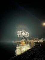 festlich Feuerwerk im das dunkel Himmel Über das Meer beim das Fuß von das Berge foto