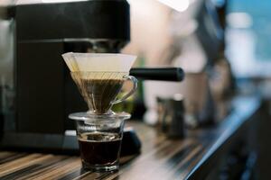 Kaffee tropft in ein Glas durch ein Filter im ein gießen Über Kaffee Hersteller auf ein Tabelle foto