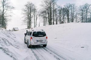 suv fährt entlang ein schneebedeckt Straße im ein Dorf. zurück Aussicht foto