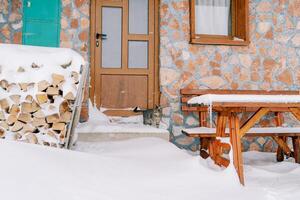 gestreift Katze steht auf das schneebedeckt Schwelle von ein Stein Haus und sieht aus beim ein Holzstapel von Brennholz foto