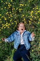 wenig Lachen Mädchen Lügen auf ein Grün Wiese mit Gelb Löwenzahn foto