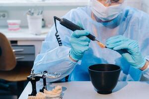 ein Dental Techniker im schützend Kleidung ist Arbeiten auf ein Prothese Zahn im seine Labor foto
