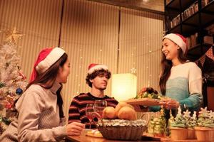 Eine besondere Mahlzeit einer Familie, junge Frau serviert gebratenen Truthahn an Freunde und fröhlich mit Getränken während eines Abendessens im Esszimmer eines Hauses, das für Weihnachtsfeste und Neujahrsfeiern dekoriert ist. foto