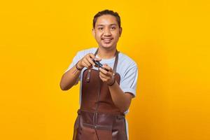 Porträt attraktiver und fröhlicher asiatischer junger Mann mit Schürze, der ein Spiel mit Joystick spielt, isoliert auf gelbem Hintergrund foto