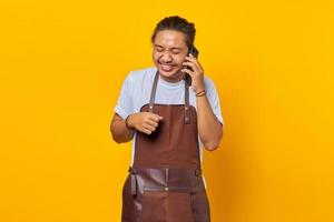 Porträt eines lachenden und fröhlichen asiatischen jungen Mannes, der auf gelbem Hintergrund auf dem Smartphone spricht foto