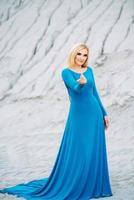 blondes Mädchen in einem blauen Kleid mit blauen Augen in einem Granitsteinbruch foto