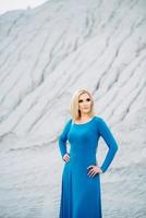 blondes Mädchen in einem blauen Kleid mit blauen Augen in einem Granitsteinbruch foto