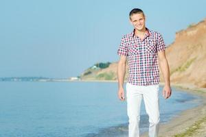 Kerl in weißen Hosen geht am Strand entlang gegen foto