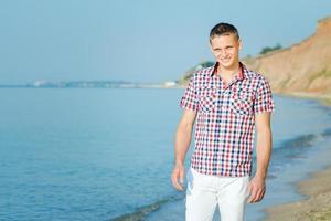 Kerl in weißen Hosen geht am Strand entlang gegen foto