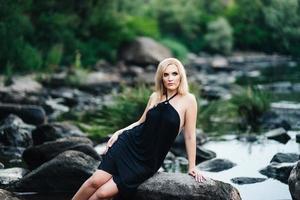 blondes Mädchen in einem schwarzen Kleid mit blauen Augen an der Küste des Flusses foto