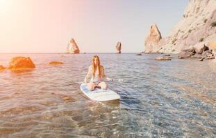 Frau Meer sup. schließen oben Porträt von glücklich jung kaukasisch Frau mit lange Haar suchen beim Kamera und lächelnd. süß Frau Porträt im ein Weiß Bikini posieren auf sup Tafel im das Meer foto