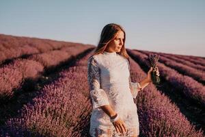 Frau Lavendel Feld. glücklich sorglos Frau im ein Weiß Kleid Gehen im ein Lavendel Feld und riechen ein Lavendel Strauß auf Sonnenuntergang. Ideal zum warm und inspirierend Konzepte im Fernweh und Reise. foto