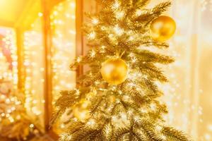 ein Weihnachten Baum mit Gold Ornamente und Beleuchtung. das Baum ist dekoriert mit Gold Bälle und ist zündete oben mit Beleuchtung. das Baum ist platziert im ein Zimmer mit ein Fenster foto