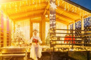 glücklich lächelnd Frau im ein Weiß Kleid halten ein Geschenk Box im Vorderseite von ein Weihnachten Baum. foto