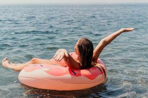 Sommer- Ferien Frau schwimmt auf ein aufblasbar Krapfen Matratze, ein Wasser Spielzeug schwimmen Ring. positiv glücklich Frau entspannend und genießen Familie Sommer- Reise Ferien Ferien auf das Meer. schleppend Bewegung foto