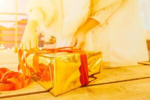 ein Frau im ein Weiß Kleid ist halten ein Gold Box mit ein rot Schleife. sie ist tragen ein Krone auf ihr Kopf. das Frau erscheint zu Sein Öffnung das Geschenk Kasten. foto