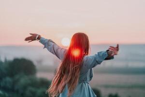 glücklich Frau Stehen mit ihr zurück auf das Sonnenuntergang im Natur im Sommer- mit öffnen Hände. romantisch schön Braut im Weiß Boho Kleid posieren mit Berge auf Sonnenuntergang foto