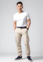 ai generiert zuversichtlich asiatisch Mann im beiläufig Weiß t Hemd und Beige Hose posieren auf ein grau Hintergrund, geeignet zum Mode und Lebensstil Konzepte foto