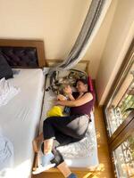 Mama und wenig Mädchen Lüge umarmen auf ein Kinder Bett in der Nähe von ein Katze foto