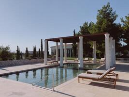 Pergola mit Säulen in der Nähe von das Schwimmbad mit Sonne Liegen umgeben durch Bäume. Hotel amanzo, Griechenland foto