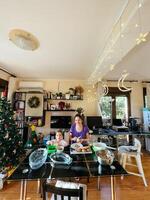 budva, Montenegro - - 25 Dezember 2022. Mama und wenig Mädchen Schnitt Gemüse Salat während Sitzung beim das Tabelle in der Nähe von das Weihnachten Baum foto
