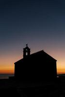 Silhouette von ein Kirche mit ein Glocke Turm auf das Dach gegen das Sonnenuntergang Himmel foto