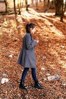 jung Frau mit ein Becher Spaziergänge durch das gefallen Blätter im das Park. Seite Aussicht foto