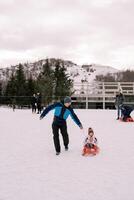 lächelnd Papa Fahrten ein klein Kind auf ein Schlitten auf ein schneebedeckt Hügel foto