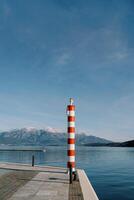 klein gestreift rot und Weiß Leuchtturm auf ein Seebrücke durch das Meer gegen das Hintergrund von Berge foto