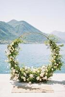 runden Hochzeit Bogen steht auf ein Seebrücke durch das Meer gegen das Hintergrund von Berge foto