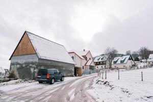 schwarz Auto steht in der Nähe von ein Haus auf das Seite von ein schneebedeckt Straße foto