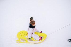 wenig lächelnd Mädchen ist Sein getragen auf ein Gelb Schlitten durch das Schnee foto