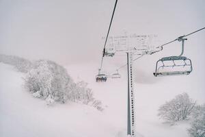 Sessellift mit Skifahrer Fahrten Über schneebedeckt Bäume zu neblig Berg foto