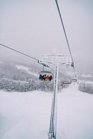 Touristen im bunt Ski Anzüge Reiten auf ein Sessellift Über ein schneebedeckt Wald bergauf foto