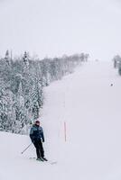 Skifahrer wendet sich auf zu ein Ski Steigung entlang ein schneebedeckt Wald foto