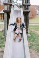 wenig Mädchen Folien Nieder ein rutschen auf ein Spielplatz halten das Handläufe foto