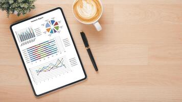 ein Digital Tablette auf ein hölzern Schreibtisch Anzeigen bunt Geschäft Analytik Grafiken neben ein Tasse von Kaffee und ein Stift. foto