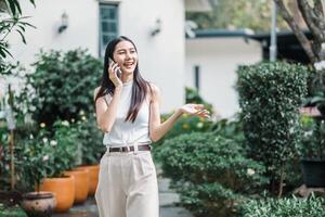 froh Geschäftsfrau hat ein angenehm Konversation auf ihr Telefon während Gehen im ein üppig Garten Einstellung. foto