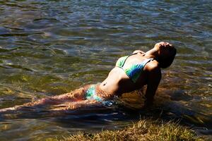 jung kaukasisch Frau im Bikini Sitzung im Fluss Wasser foto