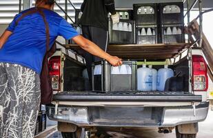 Arbeitskräfte Aufzug Weiß Trinken Wasser Flaschen im Kisten in das zurück von ein Transport LKW gereinigt Trinken Wasser Innerhalb das Produktion Linie zu bereiten zum Verkauf. Wasser trinken Fabrik, klein Geschäft foto