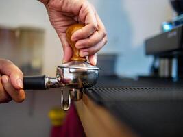 Hand von ein Barista halten ein Siebträger und ein Kaffee manipulieren Herstellung ein Espresso Kaffee. Barista drückt Boden Kaffee mit ein manipulieren im ein Kaffee Geschäft foto