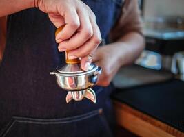 Nahaufnahme des Hand-Barista-Cafés, das Kaffee mit manuellen Pressen gemahlenen Kaffee mit Tamper im Café zubereitet foto