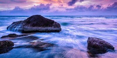 Wellen und Felsen am Strand des Sonnenuntergangs foto