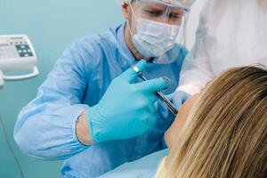 ein Zahnarzt tragen ein schützend Maske sitzt in der Nähe und hält Instrumente im seine Hände Vor Behandlung ein geduldig im das Dental Büro foto